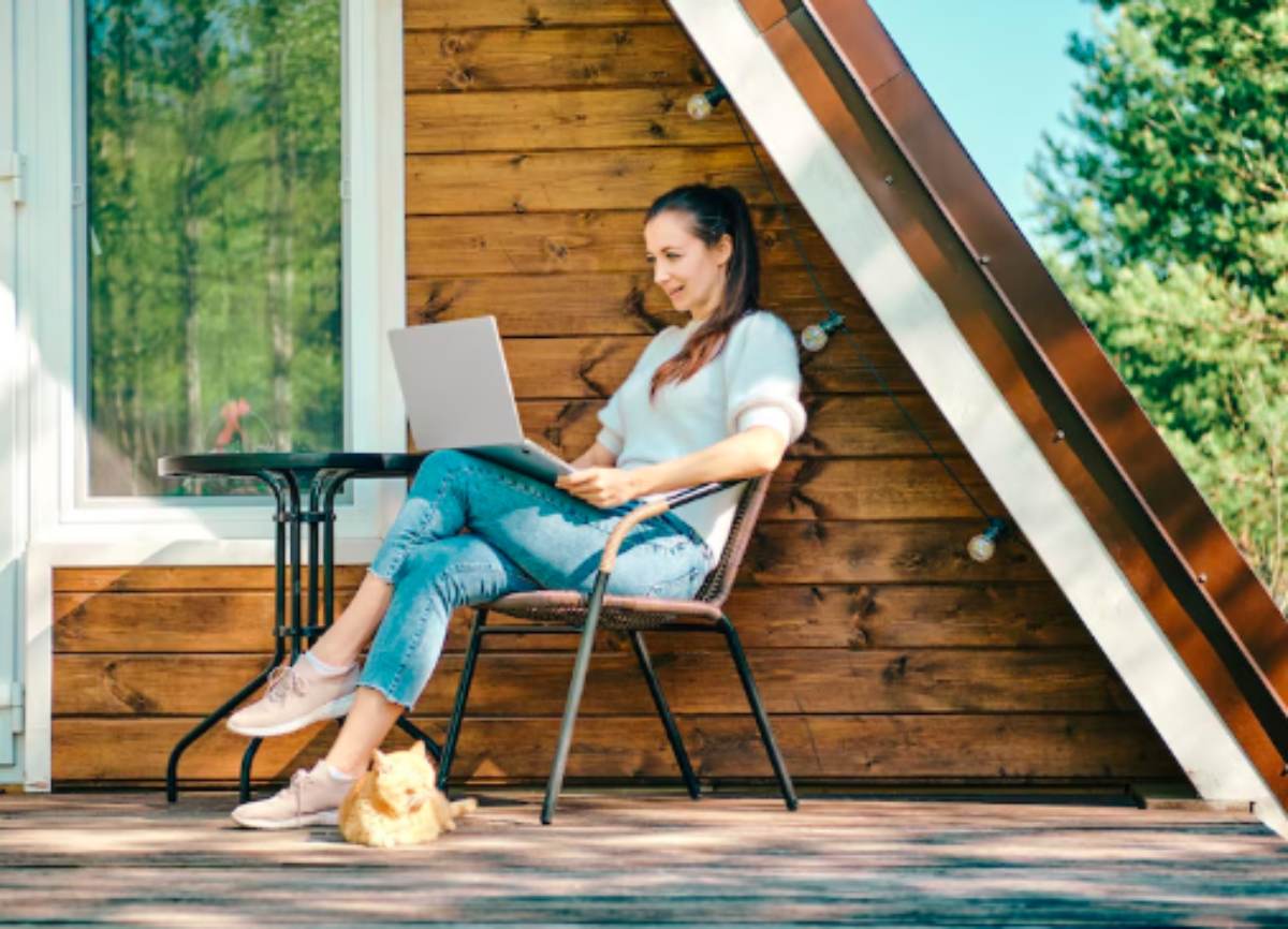 Modern garden office shed surrounded by greenery, featuring large windows, a wooden exterior, and a minimalist desk setup inside.

